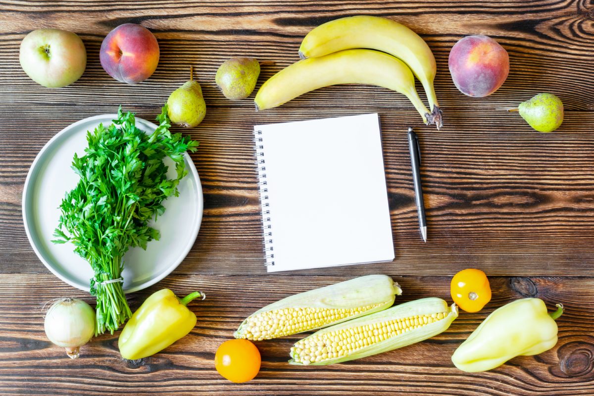 Diferentes verduras y frutas junto a una libreta en blanco encima de una mesa